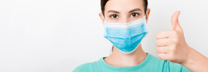 Portrait of young woman wearing medical mask at white background. Person is happy because she is...