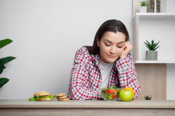 Cute woman makes a choice between healthy and harmful food