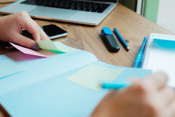 partial view of student sitting at wooden table with pen, copybook and blank sticky notes