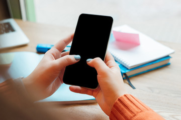 cropped view of girl holding smartphone with blank screen near books