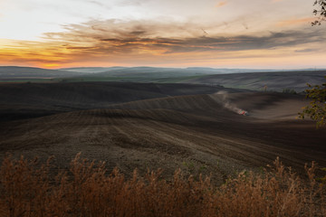 An epic panorama of Moravian fields with the setting sun where a farmer works hard with in tractor