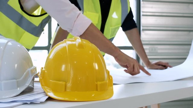 Helmets and papers on table with  background architect talking with engineer and looking  blueprint at construction site.industry concept.