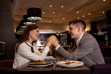 happy young caucasian couple spend their evening in restaurant, man adn woman on a date. lovely lady and handsome guy love each other, celebrate anniversary