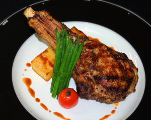 grilled Angus beef rib with potato, green beans and tomato in a white and black plate