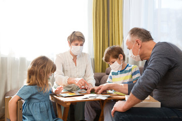 Seniors grandparents with grandsons wearing medical face mask playing  board game together at home. quarantine. health concept. Corona Virus. Family having fun playing at home. stay home concept