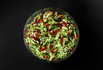 Fresh vegetable salad in a glass bowl on a dark background. Cucumbers, tomatoes, peppers. Close-up.