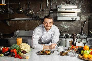 portrait of good-looking smiling cook man in the kitchen, looking at camera. posing with delicious...