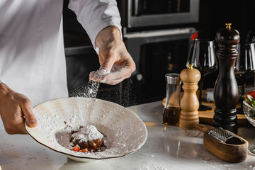 cropped cook pour powdered sugar on sweet delicious dessert. tasty food on dish. candy, culinary concept