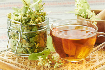 Linden herbal  tea with lime tree bloom and glass can with dried herb nearby on rustic wooden...