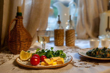 Homemade snack as of cheese cubes, cherry-tomatoes and spinach leaves, served with glass of white wine