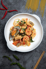 Drunken seafood spaghetti on a white plate set on a cement floor scene with fresh chilli and pepper and spaghetti lines