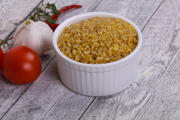 Raw bulgur in the bowl with tomatoes and garlic