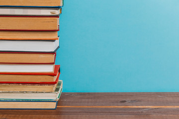 A simple composition of many hardback books, raw books on a wooden table and a bright blue background. Going back to school. Copy space. Education.