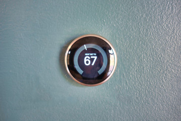 Smart thermostat isolated on light blue wall. Nest smart home technology saving money heating and cooling. Green tech saving energy