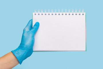 female hand in a  medical glove holds a blank form of paper on a blue background. Mock up, business...