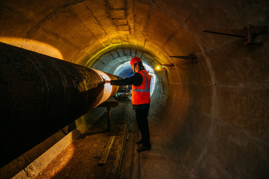 Tunnel Worker Examines Pipeline In Underground Tunnel