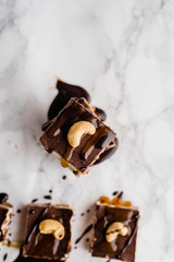 Close-up directly above of a vegan no-bake chocolate date and coconut healthy bites with peanutbutter and syrup with a cashew nut on top on white marble