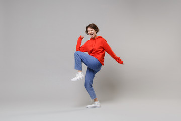 Fototapeta na wymiar Side view of happy young brunette woman girl in casual red hoodie blue jeans posing isolated on grey background. People lifestyle concept. Mock up copy space. Doing winner gesture keeping eyes closed.