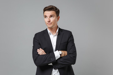 Young business man in classic black suit shirt posing isolated on grey background studio portrait. Achievement career wealth business concept. Mock up copy space. Holding hands crossed, looking aside.