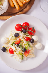 vegetables salad on the plate and plate with assorted cheese, fruit and other snacks.