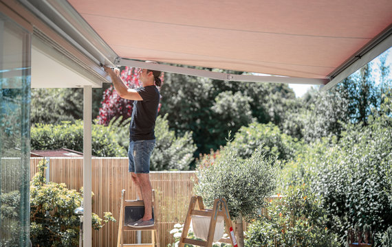 Handwerker stellt die Markise mit einem Inbus Schlüssel ein auf der Terrasse im Garten