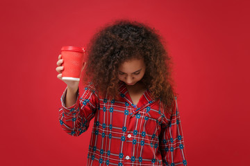 Tired young african american girl in pajamas homewear posing resting at home isolated on red background. Relax good mood lifestyle concept. Hold paper cup of coffee or tea yawning with lowered head.