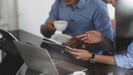 Cropped image of business developer team working together by using a computer tablet and laptop while sitting at the modern working desk over comfortable office as background.