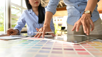 Photo of graphic designer team working together with computer tablet and color guide at the modern working table over comfortable office as background.