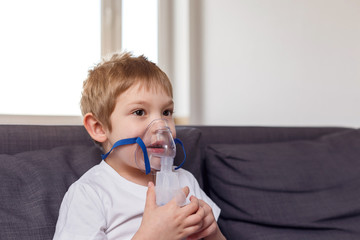 A child sits on a sofa with an inhaler at home. Coronovirus treatment concept. House insulation....
