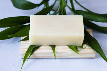 Bar of natural herbal soap on green tropical leaf on gray stone background close up eco friendly...
