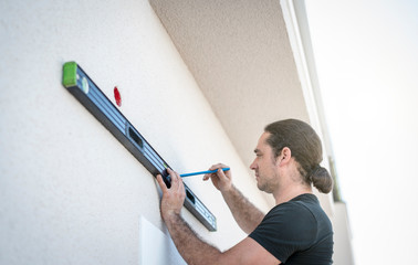 Handwerker zeichnet mit der langen Wasserwaage an der Hauswand eine Linie an