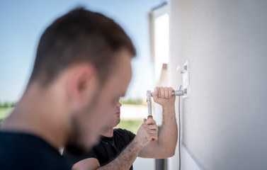 freundlicher Handwerker befestigt eine Montageplatte für eine Markise an einer Hauswand