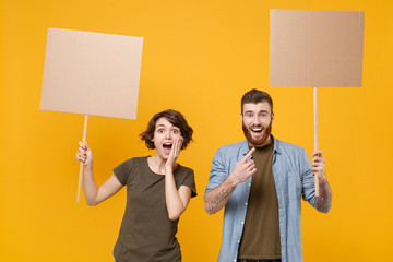 Excited protesting young two people guy girl hold protest signs broadsheet blank placard on stick isolated on yellow background studio portrait. Protests strikes pickets concept. Youth against city.
