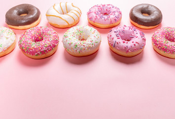 Doughnuts with multicolored glaze laid out in two rows on trendy pink background with copy space for text.