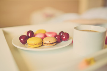 Obraz na płótnie Canvas Side view of cup of coffee with tasty colorful macarons or macaroons on white tray. Romantic breakfast concept