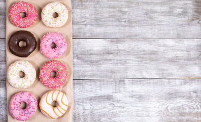 Eight traditional doughnuts with multicolored glaze on wrapping paper on white painted wooden table...