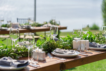 Beautifully decorated wooden table in a summer open-air cafe. Green branch and fresh flowers table decoration