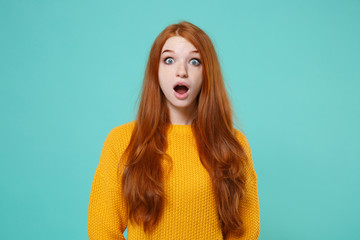 Shocked young redhead woman girl in yellow sweater posing isolated on blue turquoise wall...