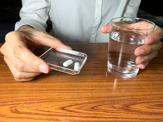 Woman holding water glass and pill in the tray. The woman are taking emergency medicine, supplements or antibiotic antidepressant painkiller medication to relieve pain.