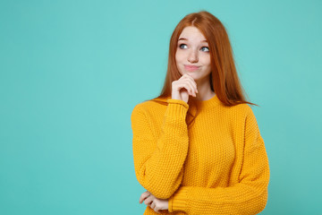 Pensive smirked young redhead woman girl in yellow sweater posing isolated on blue turquoise wall...