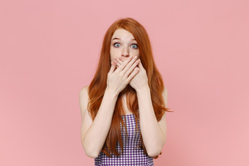Shocked young redhead woman girl in plaid dress posing isolated on pastel pink background studio portrait. People sincere emotions lifestyle concept. Mock up copy space. Covering mouth with hands.