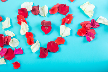 Heart of rose petals on a blue background and a heart-shaped box with jewelry.