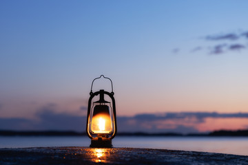 Old rusty lantern on the wet rock. Beautiful sunset sky and sea on background. Kerosene lamp soft...