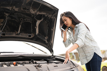 Asian young woman are stressed  and calling car insurance.Broken down car while traveling.Black long hair woman talking on cellphone after car breakdown trouble problem mechanic.