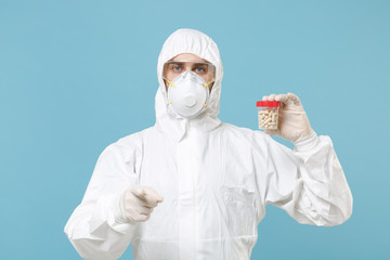 Man in white protective suit respirator mask hold jar tablets pills drugs isolated on blue background studio. Epidemic pandemic new rapidly spreading coronavirus 2019-ncov medicine flu virus concept.