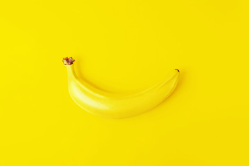 Einfarbiges gelbes Konzept. Eine einzelne frische reife Banane in der Schale auf gelbem Hintergrund. Ansicht von oben. © Antibydni