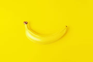 Einfarbiges gelbes Konzept. Eine einzelne frische reife Banane in der Schale auf gelbem Hintergrund. Ansicht von oben. © Antibydni