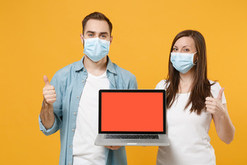 Two people in sterile face masks using laptop pc isolated on yellow background studio. Epidemic pandemic rapidly spreading coronavirus 2019-ncov medicine flu virus ill sick disease treatment concept.