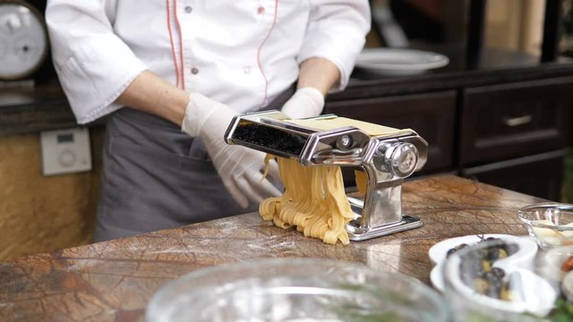 Chef's hands use a pasta cutting machine. Fresh spaghetti pasta coming out of pasta machine close up