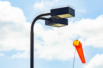 Against a partly cloudy sky two large black street lights are shown, along with an orange windsock